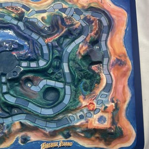 May include: A board game titled "Fireball Island" with a detailed island map design. The game board features a blue border, with a colorful island landscape in shades of green, brown, and orange. The game's title is displayed in white text.