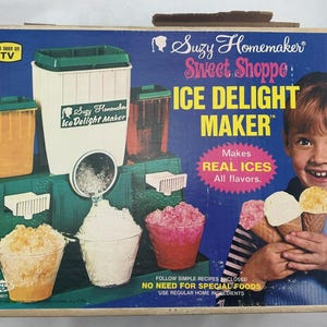 May include: Vintage Suzy Homemaker Ice Delight Maker box. The box features a young girl holding ice cream cones. The machine is green and white, with containers for ice and flavours. The text on the box reads "Makes REAL ICES All flavours."