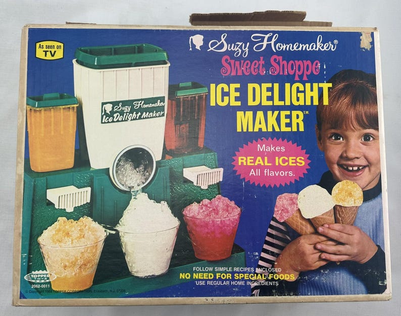 May include: Vintage Suzy Homemaker Ice Delight Maker box. The box features a young girl holding ice cream cones. The machine is green and white, with containers for ice and flavours. The text on the box reads "Makes REAL ICES All flavours."