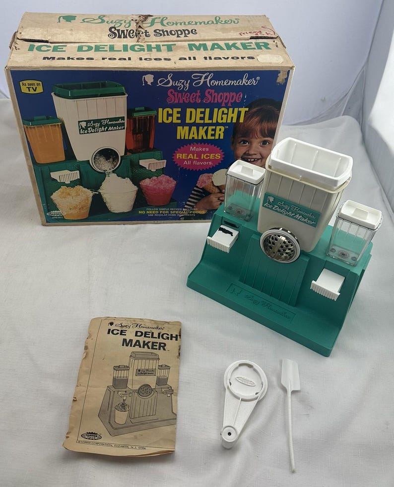 May include: A vintage Suzy Homemaker Sweet Shoppe Ice Delight Maker. The teal and white machine is accompanied by its box, manual, and accessories. The box features images of the machine in use, making ice treats. Includes a white plastic tool.