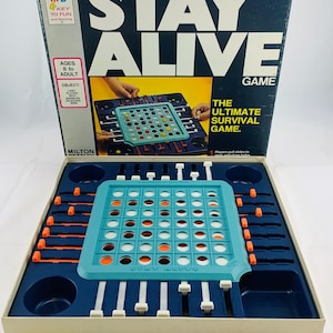 Pode incluir: Um jogo de tabuleiro vintage "Stay Alive". A caixa &eacute; azul escuro com texto branco e uma ilustra&ccedil;&atilde;o do jogo. Dentro, um tabuleiro de jogo turquesa com componentes laranja e brancos fica em uma bandeja azul marinho. Inclui pe&ccedil;as coloridas.