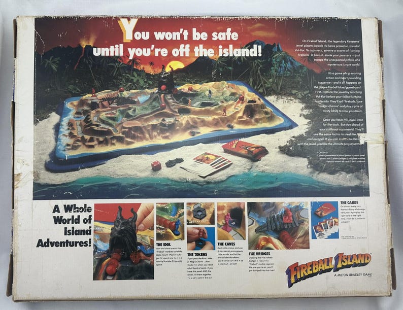 May include: Fireball Island board game box. The box features a colorful illustration of an island with a volcano, ocean, and jungle. Text on the box reads "You won't be safe until you're off the island!" and "A Whole World of Island Adventures!"