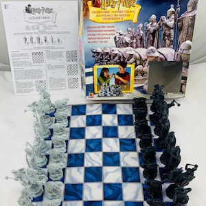 May include: A Harry Potter Wizard Chess set featuring a blue and white marbled game board, a set of white chess pieces, a set of black chess pieces, an instruction sheet, and a large cardboard box with the Harry Potter logo and game imagery.