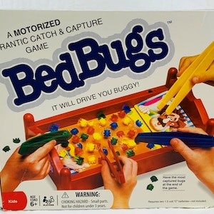 May include: A boxed "Bed Bugs" game with a red bed-shaped game board. The box reads "A Motorized Frantic Catch & Capture Game". The game includes colorful plastic bugs and tweezers. The game is for ages 6+.