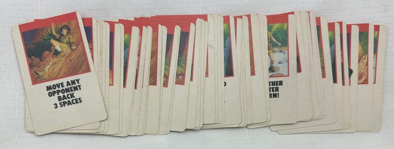 May include: A deck of vintage game cards with red borders and illustrations. One card reads "MOVE ANY OPPONENT BACK 3 SPACES." The cards feature various images and text, suggesting a board game or card game.