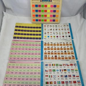 May include: A beige plastic educational computer toy with a grid of colorful square buttons, accompanied by five double-sided learning cards featuring multiplication tables, animal illustrations, and national flags with their respective country names.