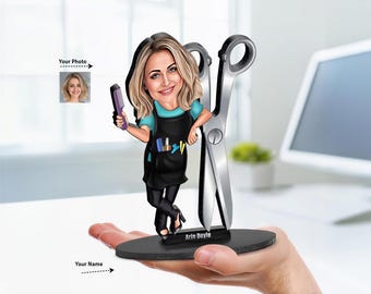 May include: A custom caricature figurine of a hairstylist with blonde hair, wearing a teal shirt and black apron, holding a purple comb. The figure leans against a large pair of silver scissors on a black oval base with the name Arin Doyle printed.