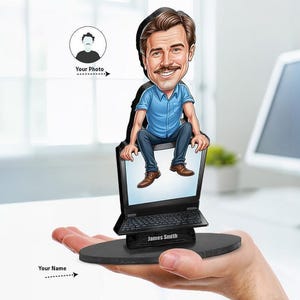 May include: A custom caricature figurine featuring a cartoon-style person with brown hair and a mustache, wearing a blue shirt and dark pants, sitting on top of a black laptop. The base includes the printed name James Smith on a black stand.