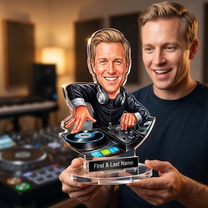 May include: A clear acrylic DJ caricature featuring a smiling man with headphones and a black shirt. The caricature is holding a turntable and mixer. The base of the acrylic has the text "First & Last Name".