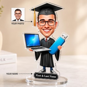 Könnte beinhalten: Ein personalisierter Acryl-Aufsteller mit einem Comic-Absolventen in schwarzer Robe und Doktorhut, Brille und Turnschuhen. Die Figur hält einen silbernen Laptop und einen blauen USB-Stick. Der Sockel trägt den Text First & Last Name.