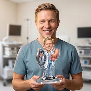 Può includere: Una figura in acrilico in stile cartone animato di un medico che tiene in mano uno strumento medico e uno stomaco. La figura è su una base trasparente con la scritta "First & Last Name". Il medico indossa un camice bianco e un camice blu.