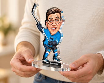 May include: A custom acrylic cutout of a cartoon hockey player wearing a blue jersey with the number 17, black gloves, and skates. The figure holds a hockey stick and stands on a clear base with the name Mara Demir printed in white text.