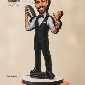 Könnte beinhalten: Eine personalisierte Karikatur-Figur eines Barkeepers mit schwarzer Weste, weißem Hemd und schwarzer Fliege. Die Figur hält einen silbernen Cocktailshaker und ein Martiniglas mit Orangenscheibe und steht auf einem Sockel mit der Aufschrift First Name & Last Name.