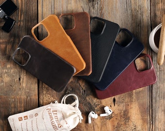 Op de afbeelding: Zes verschillende gekleurde leren telefoonhoesjes in een halve cirkel op een houten oppervlak. De hoesjes zijn allemaal gemaakt van hoogwaardig leer en hebben een verscheidenheid aan kleuren, waaronder bruin, zwart, blauw en rood. De hoesjes zijn allemaal ontworpen om op een smartphone te passen en hebben een uitsparing voor de camera lens. De hoesjes zijn allemaal gemaakt door Leathers Personalized.
