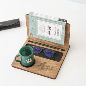 May include: A wooden book stand with a book titled "Araba Sevdasi" by Recaizade Mahmut Ekrem. The stand also has a cup of tea, a pair of glasses, and a pencil. The stand is personalised with the name "Samantha Wilson".