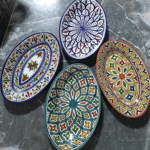 Könnte beinhalten: Vier ovale Keramikteller mit komplizierten geometrischen Mustern in Blautönen, Grün, Gelb, Rot und Weiß. Die Teller sind mit traditionellen marokkanischen Mustern verziert.