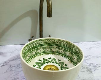May include: A white ceramic sink with a green geometric pattern and a brass drain. The sink is on a white marble countertop.