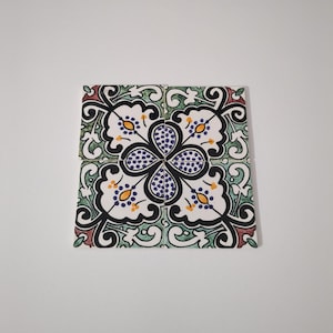 May include: Four square ceramic tiles arranged together, featuring a floral design. The tiles have a white background with a black, green, and red floral pattern. The center of the design is a dark blue flower with yellow accents.