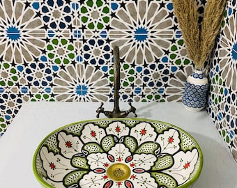May include: Oval ceramic sink with a green, white, and red floral design. The sink has a gold drain and is set against a background of blue and green patterned tiles.
