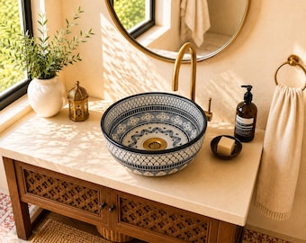 Puede incluir: Un lavabo de recipiente redondo de cerámica con un detallado patrón geométrico en blanco y negro tanto en el interior como en el exterior, junto a un grifo dorado y un desagüe a juego, sobre una encimera de piedra de color claro.