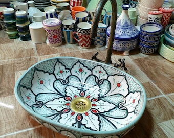 May include: A decorative ceramic sink with a floral design in shades of blue, green, white, and red. The sink has a gold drain and is oval shaped.