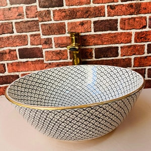 May include: A white ceramic sink with a black and white geometric pattern and a gold rim. The sink is round and has a slight curve to the bottom.