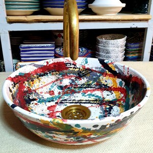 May include: A white ceramic sink with a colorful abstract design. The sink has a brass drain and a brass faucet.