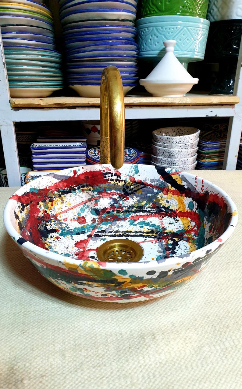 May include: A white ceramic sink with a colorful abstract design. The sink has a brass drain and a brass faucet.