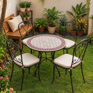 Può includere: Un tavolo da bistrot rotondo con piano in mosaico dal motivo geometrico beige e bordeaux, accompagnato da quattro sedie in metallo nero con schienali a volute e cuscini beige fissati con lacci in tessuto su un prato verde.