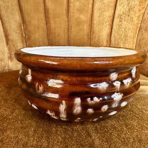 May include: A brown ceramic planter with a white interior. The exterior features a glossy finish with a dripped white pattern. The planter has a rounded shape with horizontal ridges.