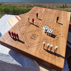 May include: A wooden baseball game with red and white pegs, two dice, and a scorecard. The game board is engraved with "Let's Play Ball!" and has a baseball diamond design.