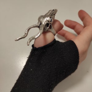 Könnte beinhalten: Ein silberner Ring mit einem detaillierten Totenkopfdesign, getragen an einem Finger mit einem schwarzen Fingerlos-Handschuh.