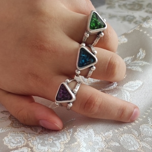Puede incluir: Tres anillos de plata con piedras de forma triangular. Las piedras son verdes, azules y moradas.
