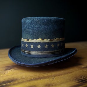 May include: A dark blue top hat with a band of white stars on a dark blue background. The hat is sitting on a wooden surface.
