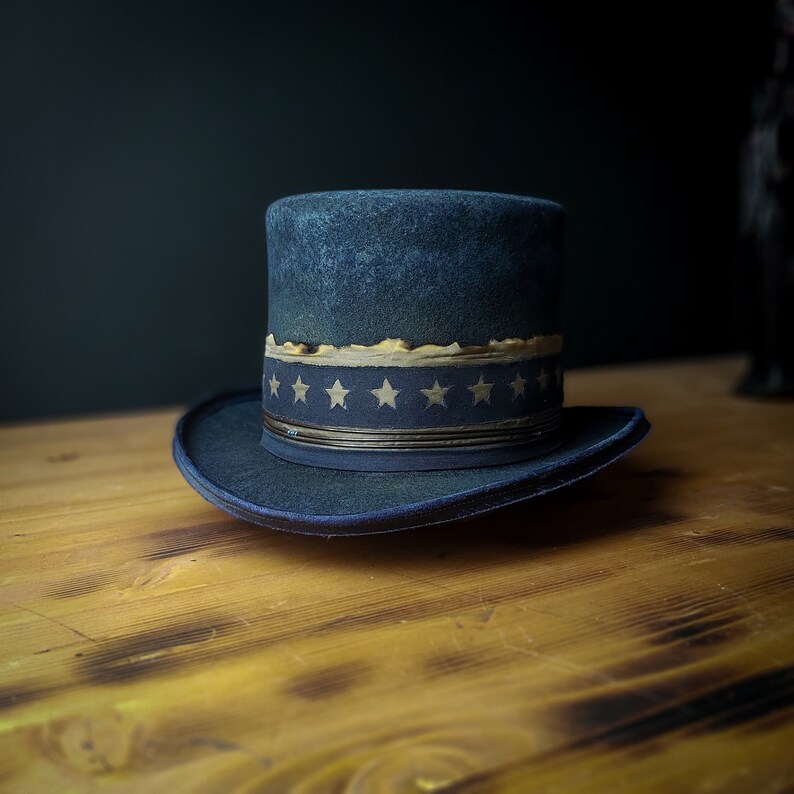 May include: A dark blue top hat with a band of white stars on a dark blue background. The hat is sitting on a wooden surface.