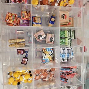May include: A clear plastic organizer filled with miniature food items. The items include boxes of Jell-O, Bagel Bites, and Pizza Hut boxes. There are also miniature bottles of juice, ketchup, and other packaged goods.