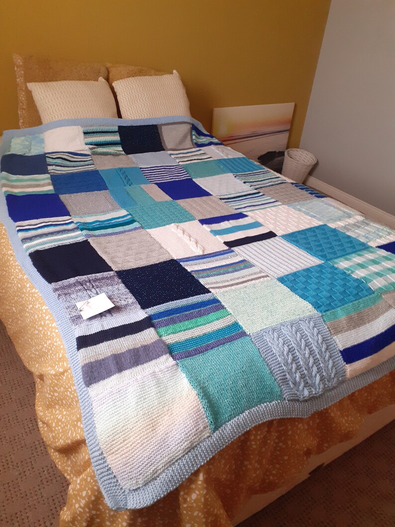 Pu&ograve; includere: Una coperta patchwork di maglia blu e bianca con un bordo blu chiaro. La coperta &egrave; realizzata con diversi quadrati di tessuto a maglia in varie tonalit&agrave; di blu, bianco e grigio.