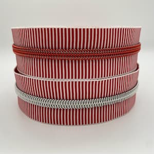 Könnte beinhalten: Ein Stapel rot-weiß gestreifter Geschenkbandrollen. Die Rollen sind mit rotem und silbernem Draht verziert. Das Band ist eng gewickelt, wodurch ein ordentliches Aussehen entsteht. Die Gesamtästhetik ist sauber und ansprechend.