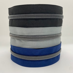 Könnte beinhalten: Ein Stapel aus drei Reißverschlussbändern in Schwarz, Grau und Blau mit silbernen Metallzähnen.
