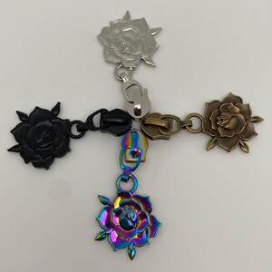 Könnte beinhalten: Vier Reißverschluss-Zipper mit Rosenmotiven. Ein Zipper ist silber, einer ist schwarz, einer ist bronzefarben und einer ist regenbogenfarben.