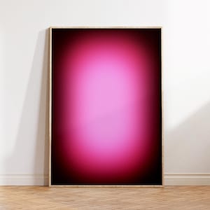 Peut inclure: Une œuvre d'art murale rectangulaire dans un cadre en bois clair présentant un design en dégradé. Le centre affiche une teinte rose vive et éclatante qui se fond dans un noir profond sur les bords, créant un effet lumineux flou.