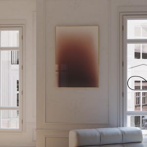 May include: A stylish living room interior featuring a framed abstract artwork with a brown and beige gradient. A light grey sofa is positioned near a large window. The room has hardwood flooring and a minimalist design. The artwork is framed in gold.
