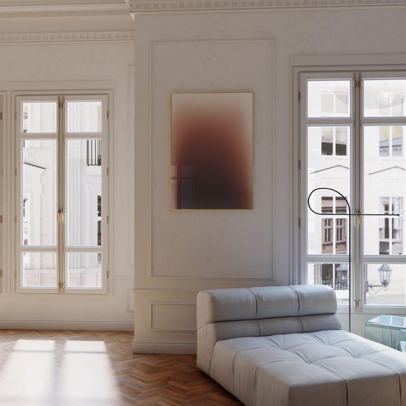 May include: A stylish living room interior featuring a framed abstract artwork with a brown and beige gradient. A light grey sofa is positioned near a large window. The room has hardwood flooring and a minimalist design. The artwork is framed in gold.