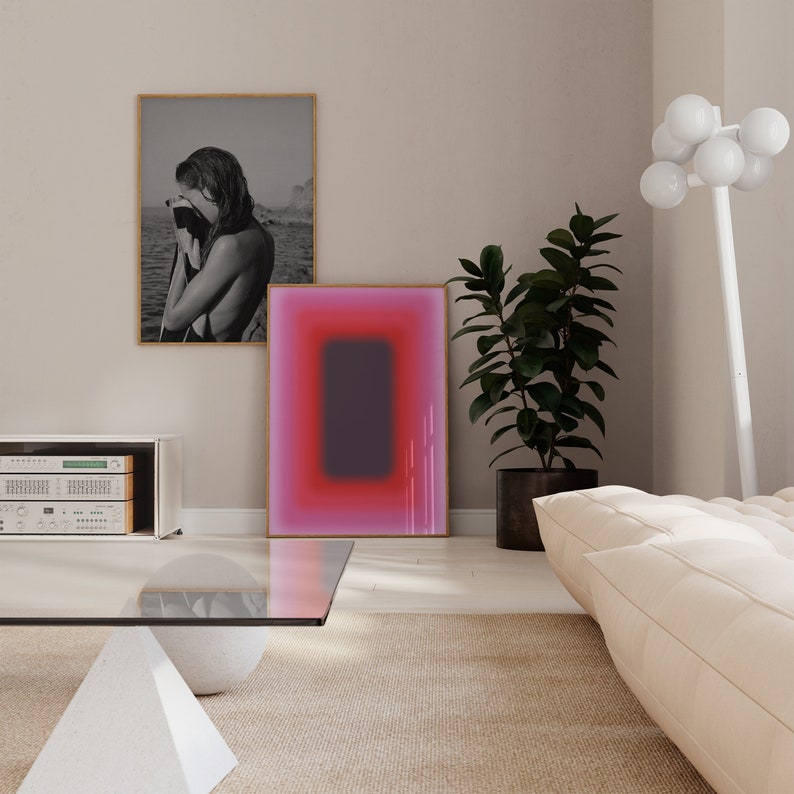 May include: A living room interior with a white sofa, a glass coffee table, a potted plant, and two framed pictures on the wall. One picture is a black and white photograph of a woman, and the other is a pink and purple abstract painting.