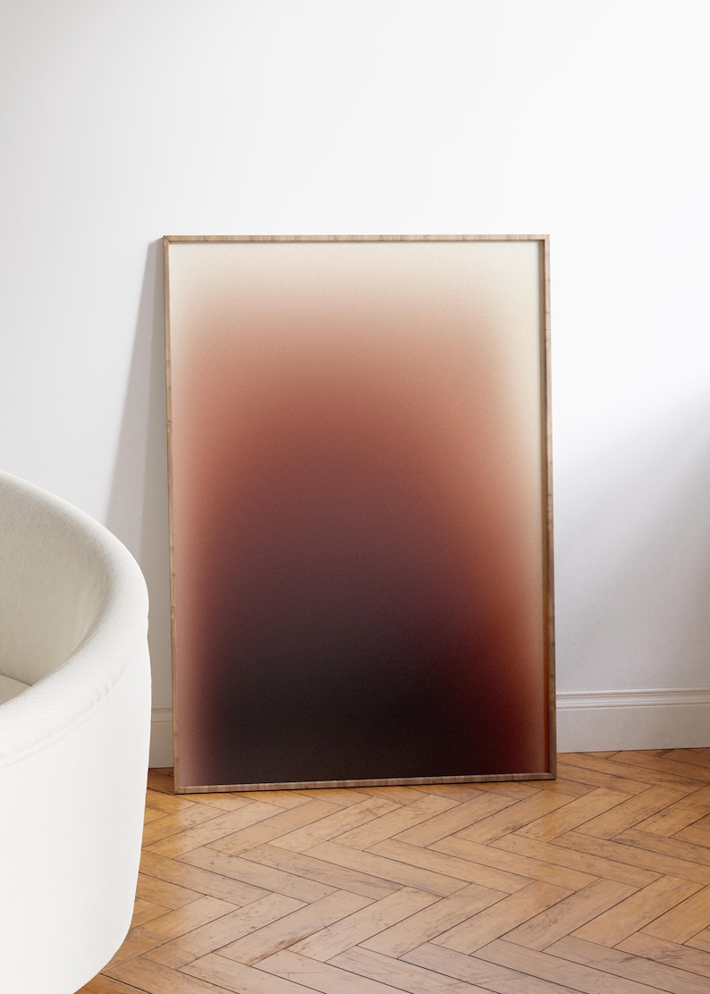 May include: A framed artwork with a gradient design. The colour transitions from a light beige at the top to a deep burgundy at the bottom. The frame is a light brown colour. The artwork is leaning against a white wall.