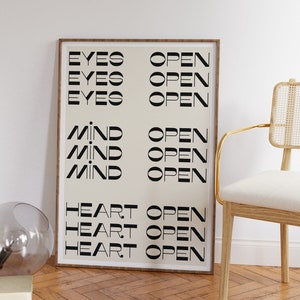 May include: A framed print with the words "Eyes Open", "Mind Open", and "Heart Open" repeated three times in black text on a cream background.