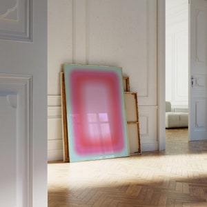 Puede incluir: Una impresión de arte abstracto enmarcada con un degradado de colores rosa, rojo y azul. La impresión se apoya contra una pared blanca en una habitación con suelo de madera.