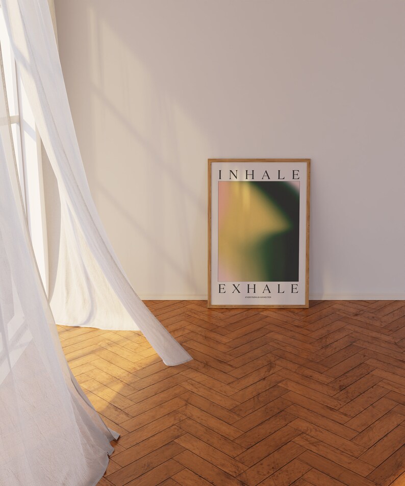 May include: A framed poster with the words "INHALE" and "EXHALE" in a minimalist font. The artwork features a blurred gradient of pink, yellow, and green. The poster is displayed on a wooden floor, next to a sheer white curtain.