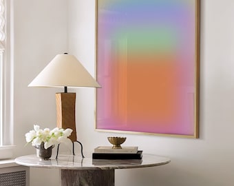 May include: A round marble table with a wooden base and a lamp with a white shade. There are two white stools and a framed abstract art print with a gradient of pink, orange, yellow, green, and blue colours. The table has a stack of books and a small gold bowl on top.