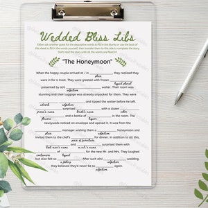 Puede incluir: Una tarjeta de juego imprimible con el título "Wedded Bliss Libs" e instrucciones para completar los espacios en blanco con palabras descriptivas para completar una historia sobre una luna de miel. La tarjeta presenta un diseño floral verde.